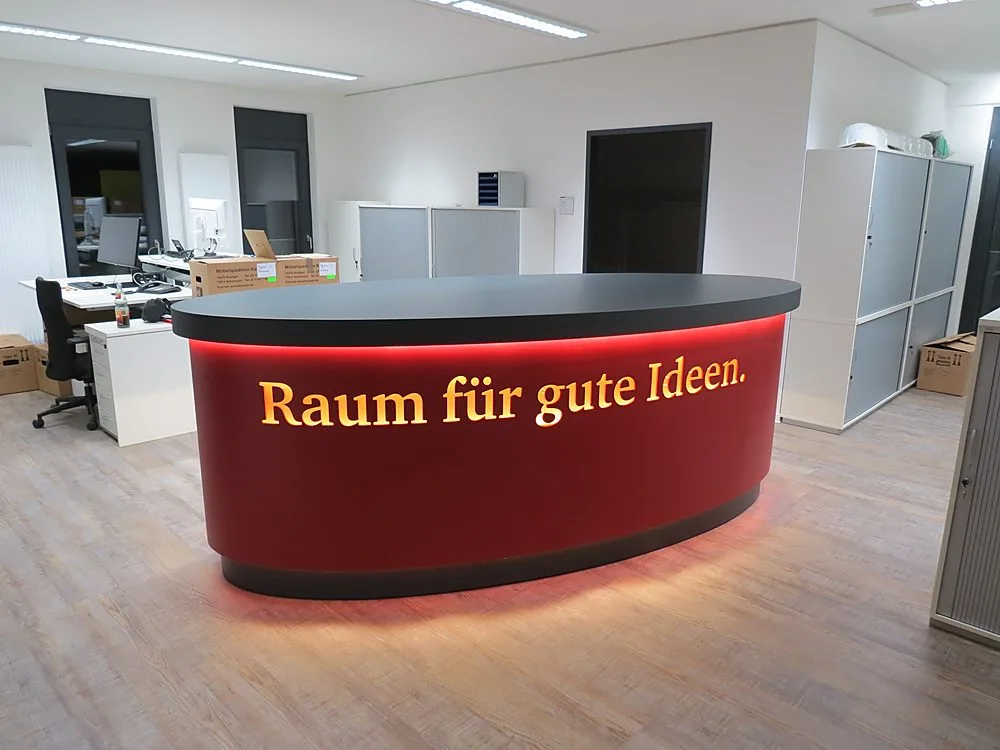 Ovale Empfangstheke mit beleuchteter roter Front – Schreinerei Hübl